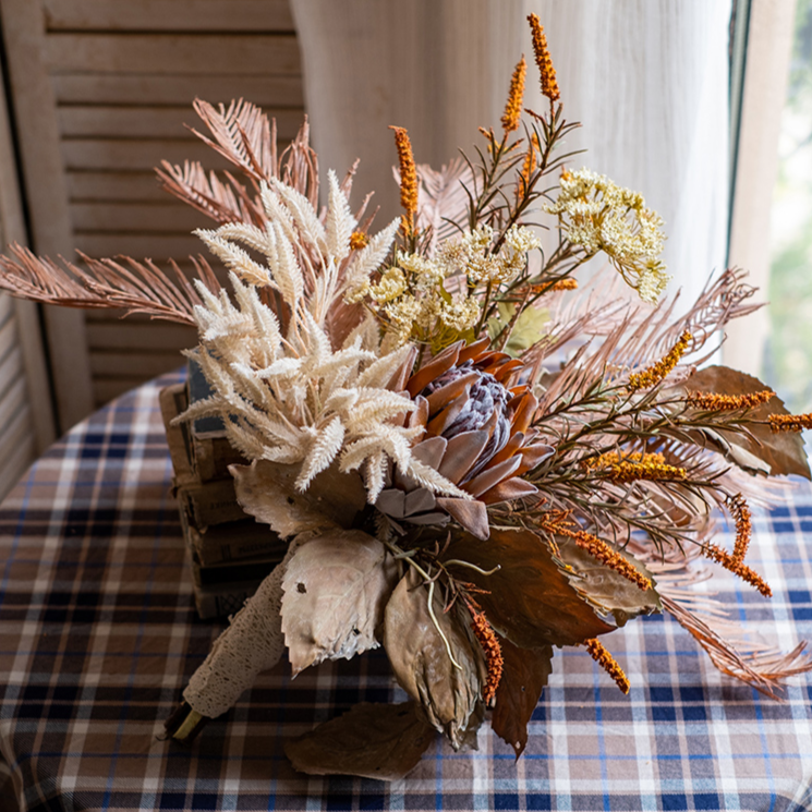 A beautifully arranged Artificial Silk Natural Fall Designer Flower Bouquet featuring protea and fern plants in white, purple, and light brown colors.