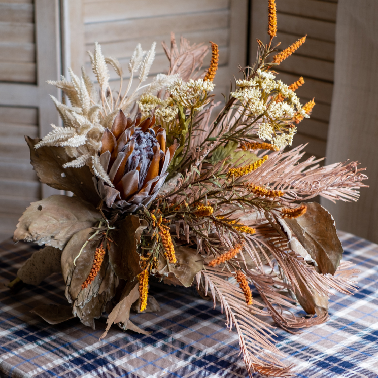 A beautifully arranged Artificial Silk Natural Fall Designer Flower Bouquet featuring protea and fern plants in white, purple, and light brown colors.