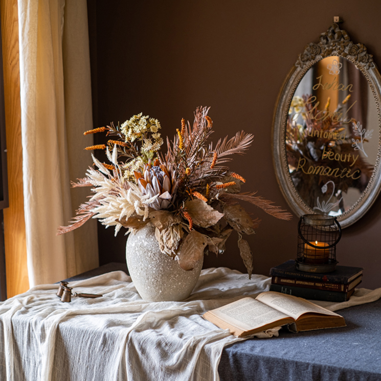 A beautifully arranged Artificial Silk Natural Fall Designer Flower Bouquet featuring protea and fern plants in white, purple, and light brown colors.