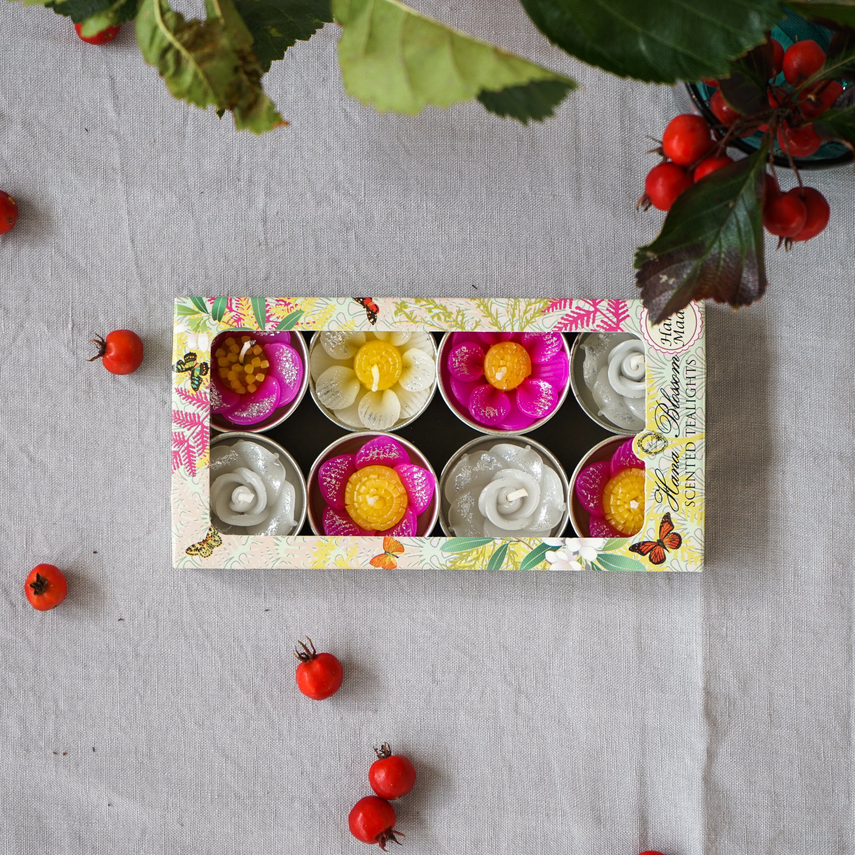 A collection of assorted glitter flower scented tealights in white, pink, and yellow, beautifully arranged in a botanic garden printed box.