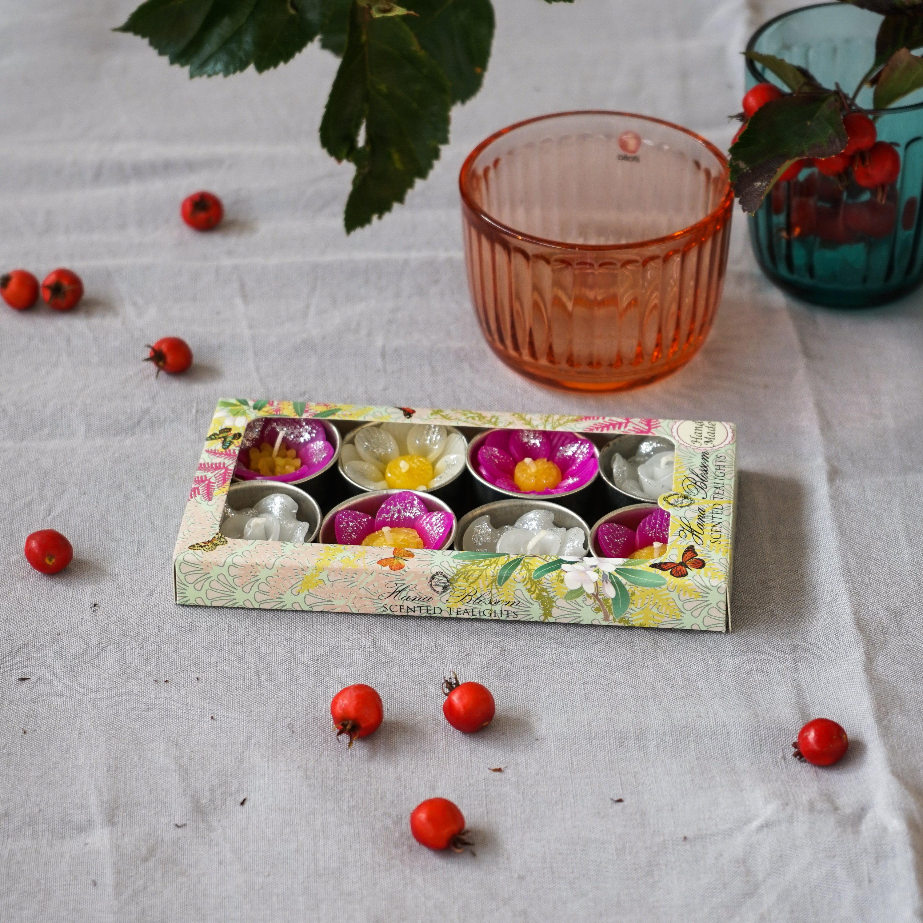 A collection of assorted glitter flower scented tealights in white, pink, and yellow, beautifully arranged in a botanic garden printed box.