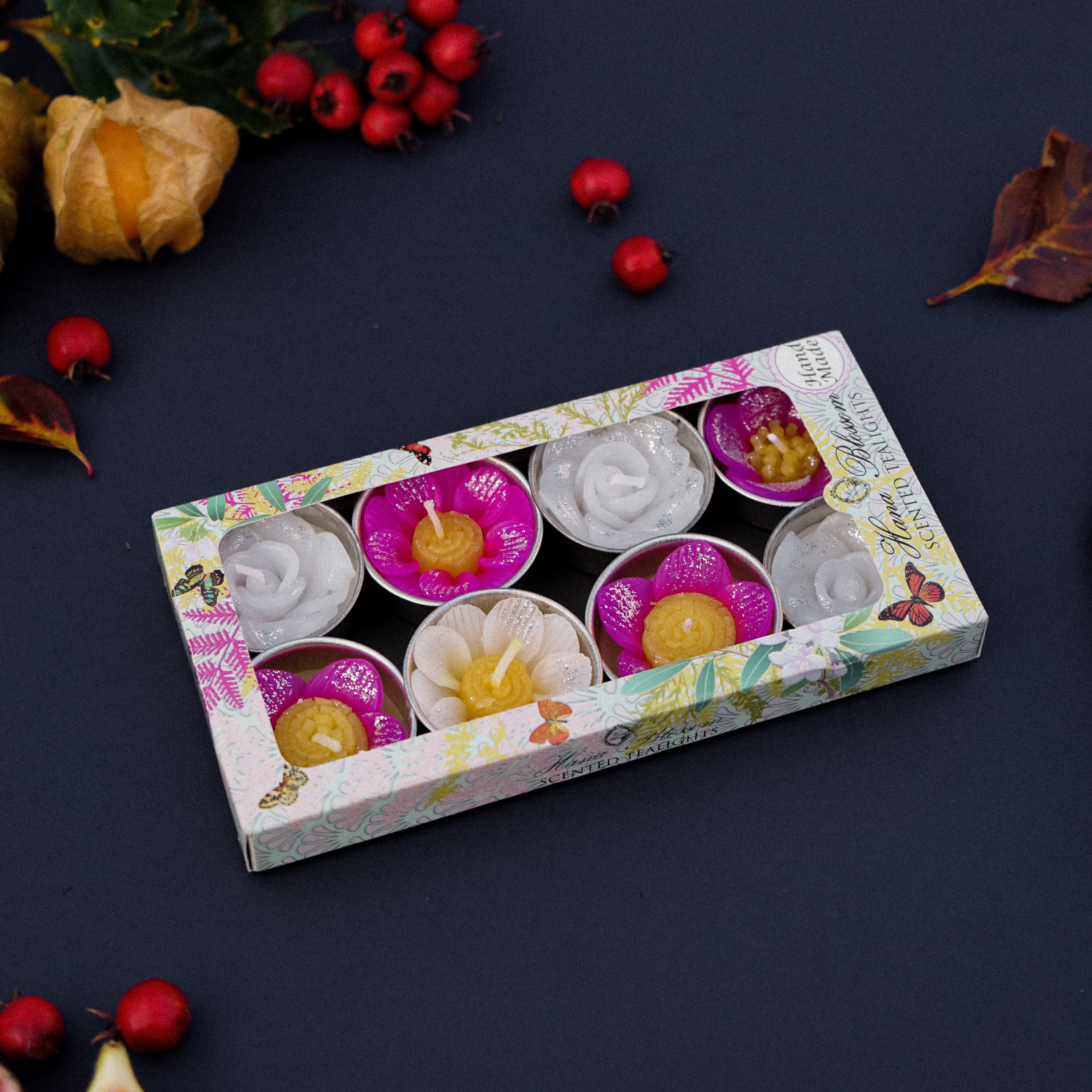 A collection of assorted glitter flower scented tealights in white, pink, and yellow, beautifully arranged in a botanic garden printed box.