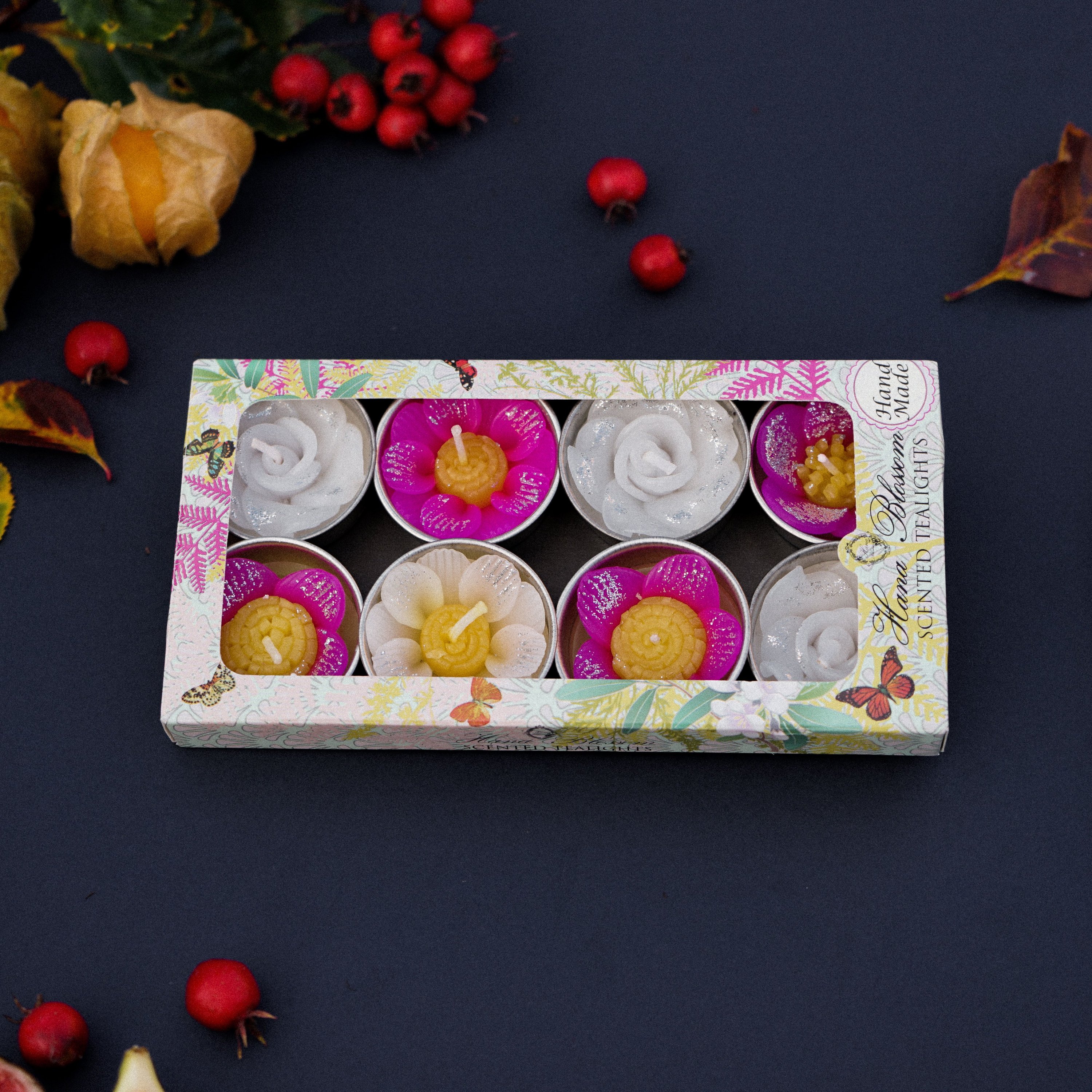 A collection of assorted glitter flower scented tealights in white, pink, and yellow, beautifully arranged in a botanic garden printed box.