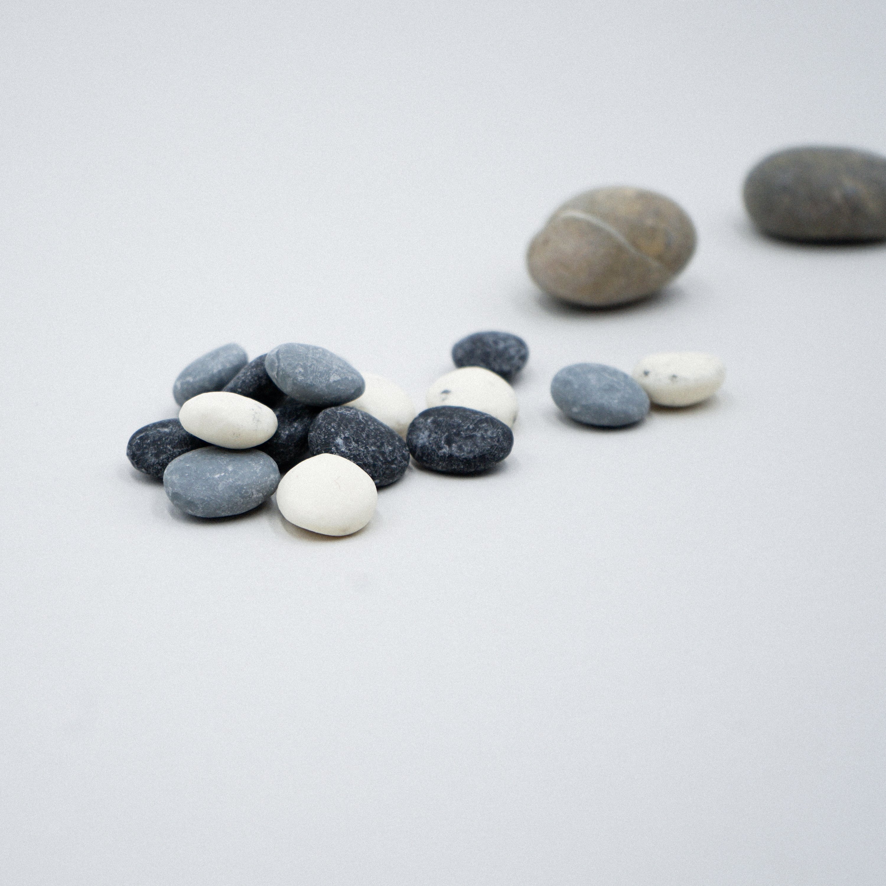 A set of assorted small pebble soaps in various colors displayed on a white porcelain dish with a grey marble effect.