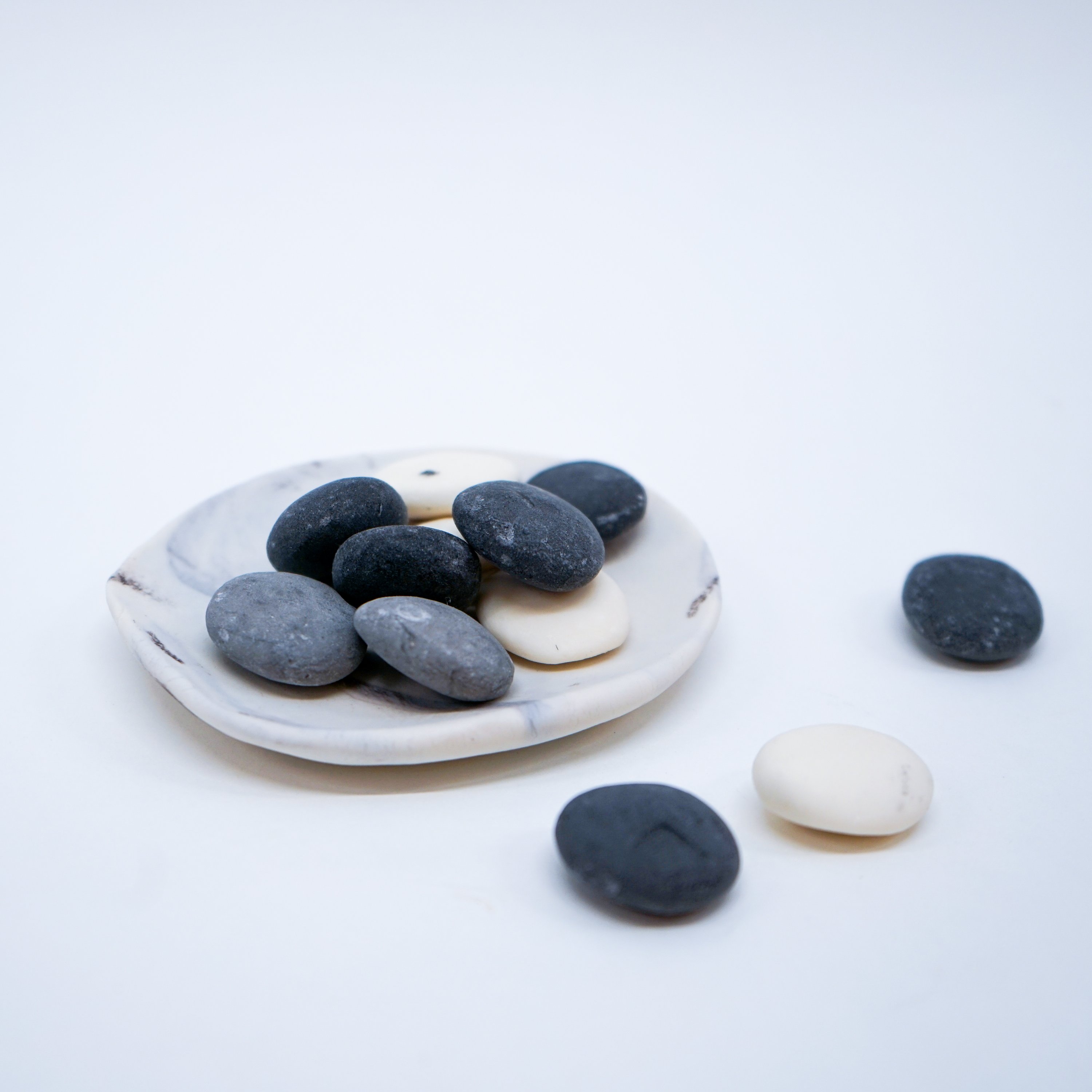 A set of assorted small pebble soaps in various colors displayed on a white porcelain dish with a grey marble effect.