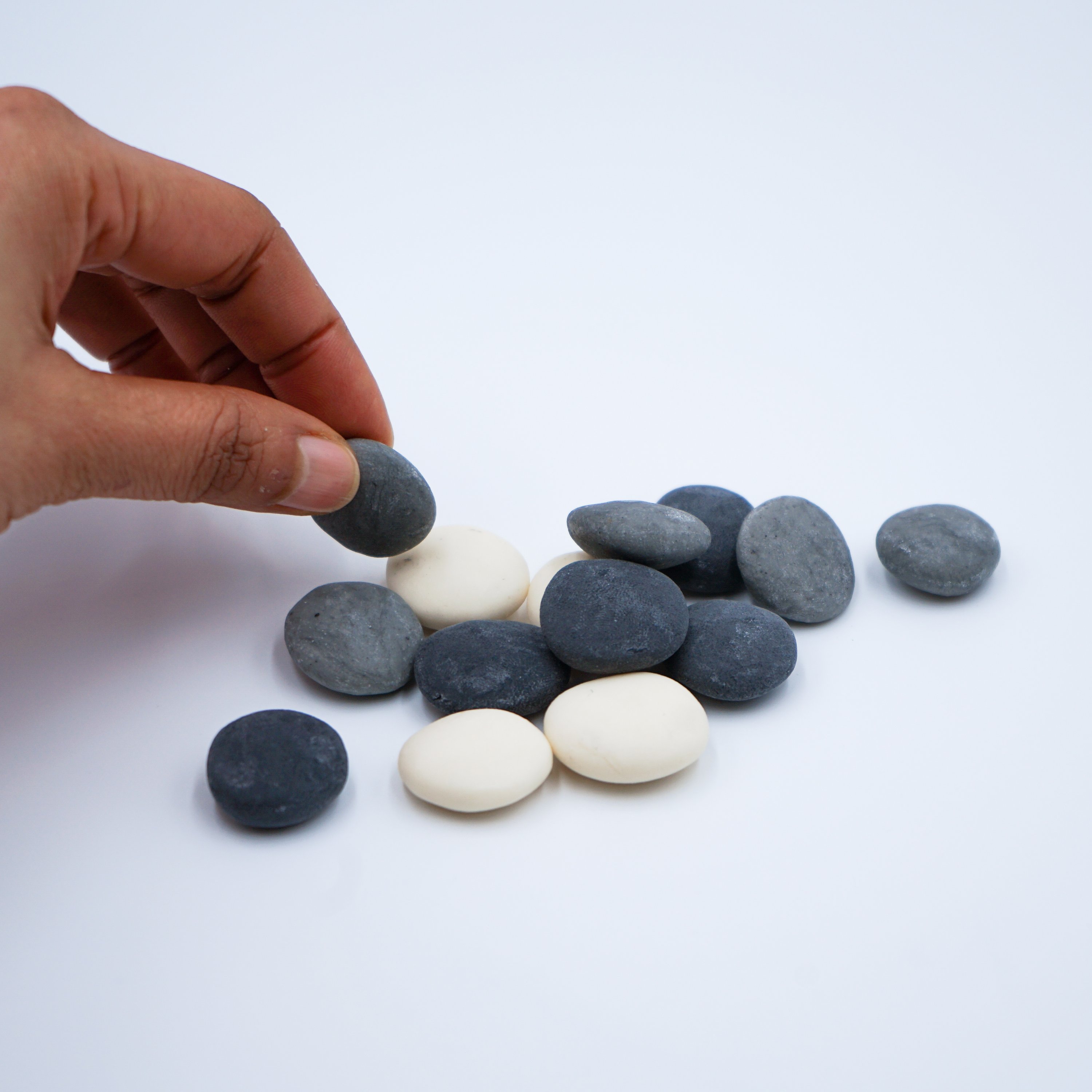 A set of assorted small pebble soaps in various colors displayed on a white porcelain dish with a grey marble effect.