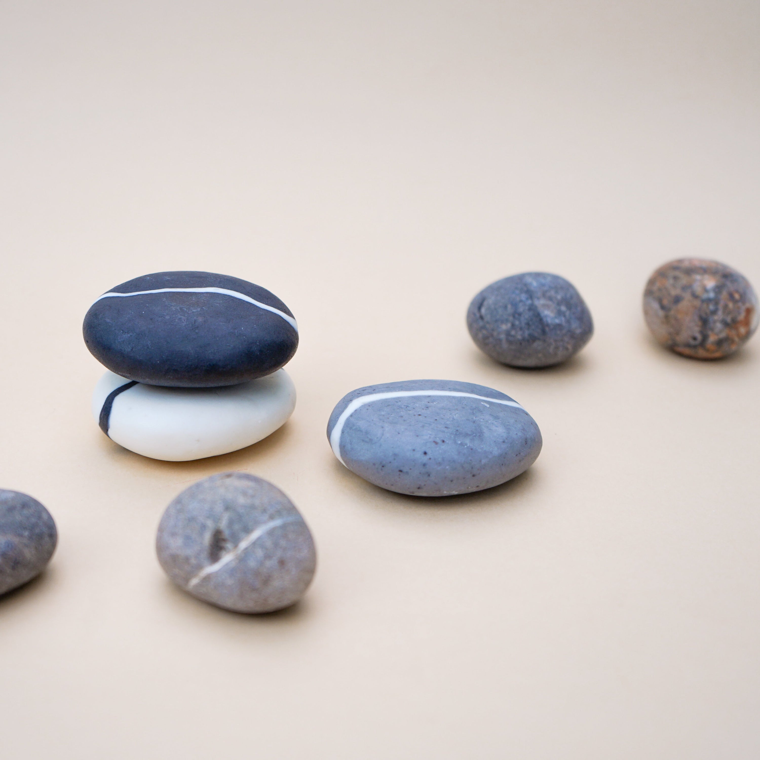 A set of three handmade pebble-shaped soaps in charcoal, grey, and white with a stylish stripe design, showcasing their natural beauty.