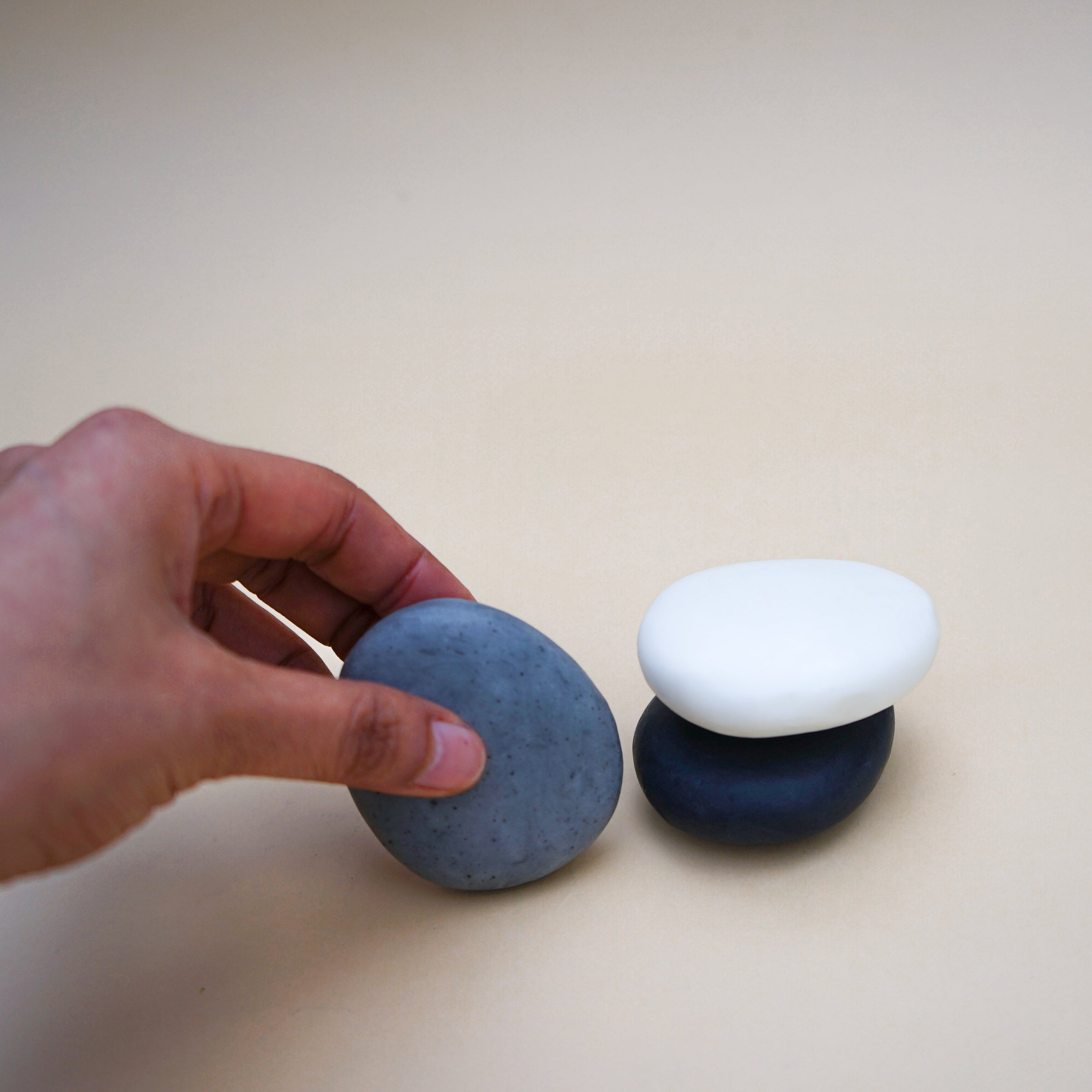 A set of three handmade pebble-shaped soaps in charcoal, grey, and white with a stylish stripe design, showcasing their natural beauty.