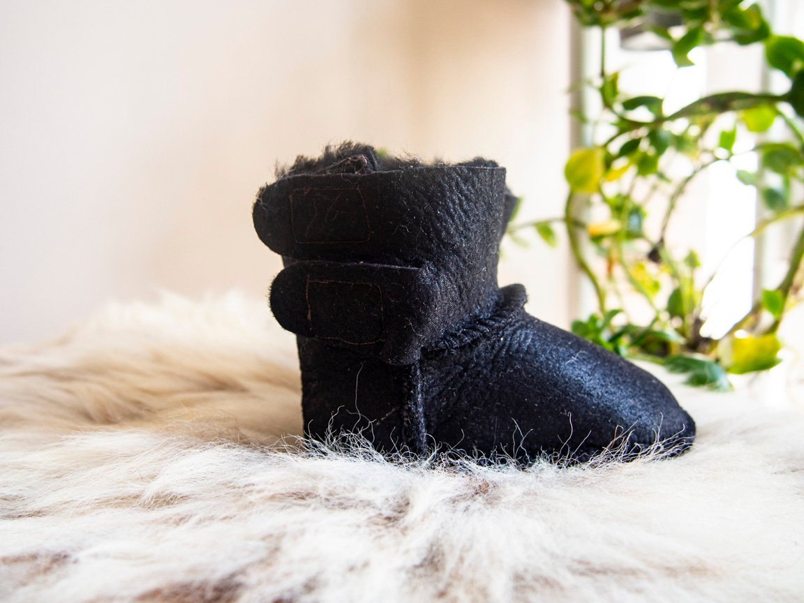 A pair of handmade baby black sheepskin boots with soft fur lining, featuring velcro fastenings for easy wear.