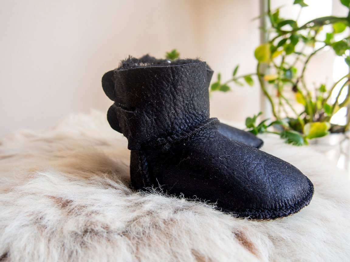 A pair of handmade baby black sheepskin boots with soft fur lining, featuring velcro fastenings for easy wear.