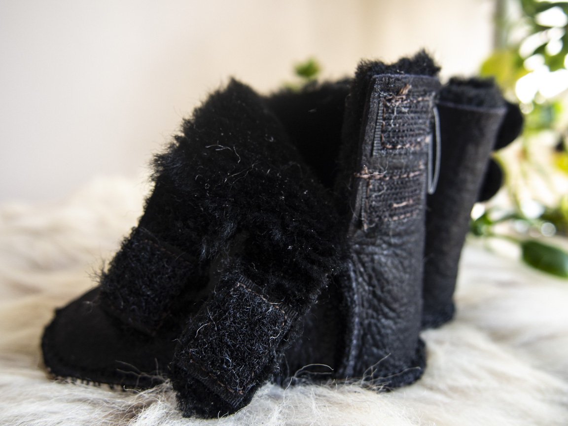 A pair of handmade baby black sheepskin boots with soft fur lining, featuring velcro fastenings for easy wear.