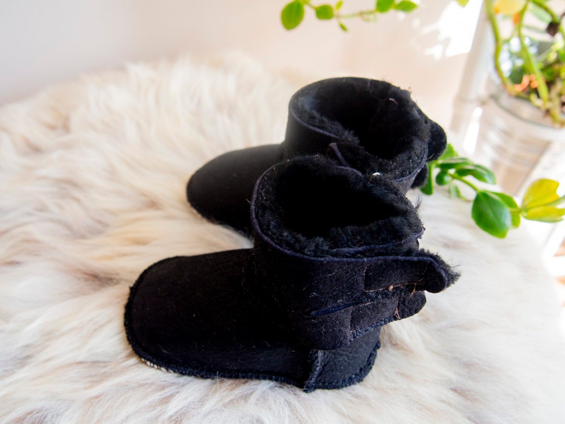 A pair of handmade baby black sheepskin boots with soft fur lining, featuring velcro fastenings for easy wear.