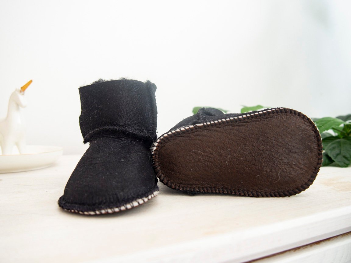 A pair of handmade baby black sheepskin boots with soft fur lining, featuring velcro fastenings for easy wear.