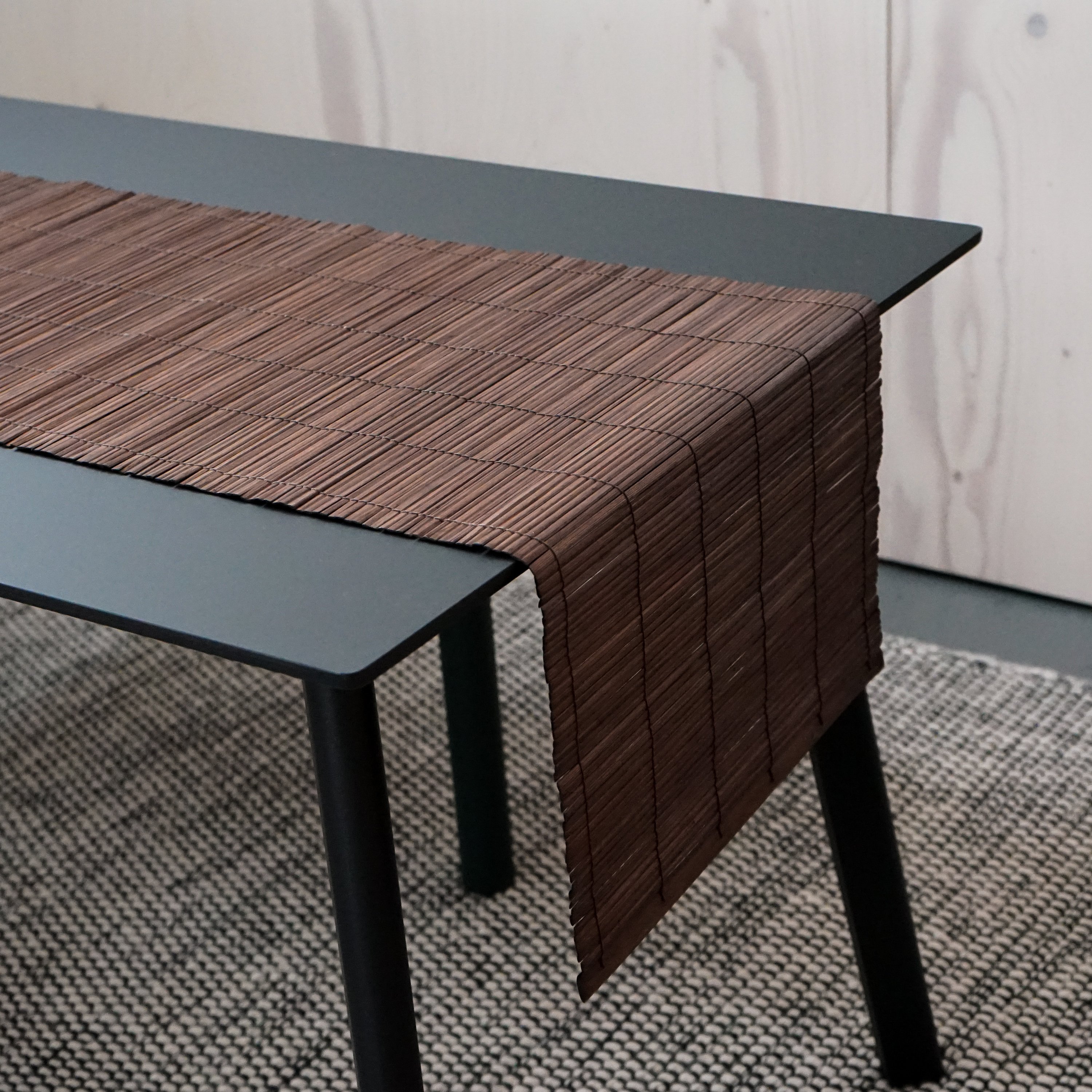 A beautifully handcrafted bamboo table runner in rich brown color, elegantly draped over a dining table, showcasing its natural texture and design.