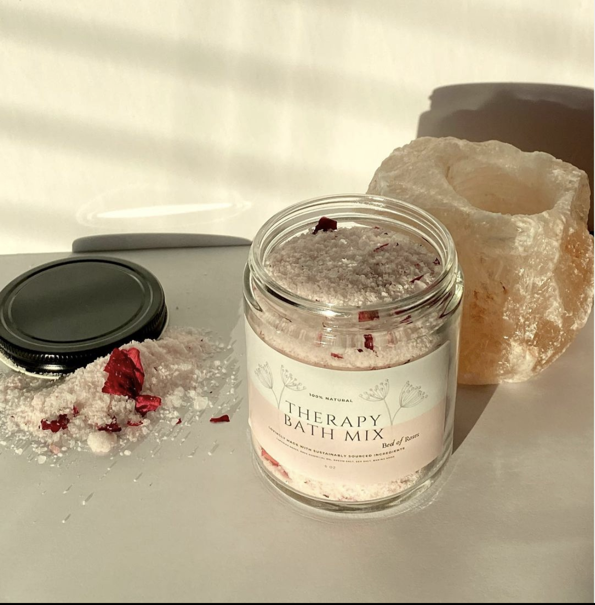 A jar of Bed of Roses Therapy Bath Mix with rose petals and essential oil, showcasing its floral aroma and luxurious experience.