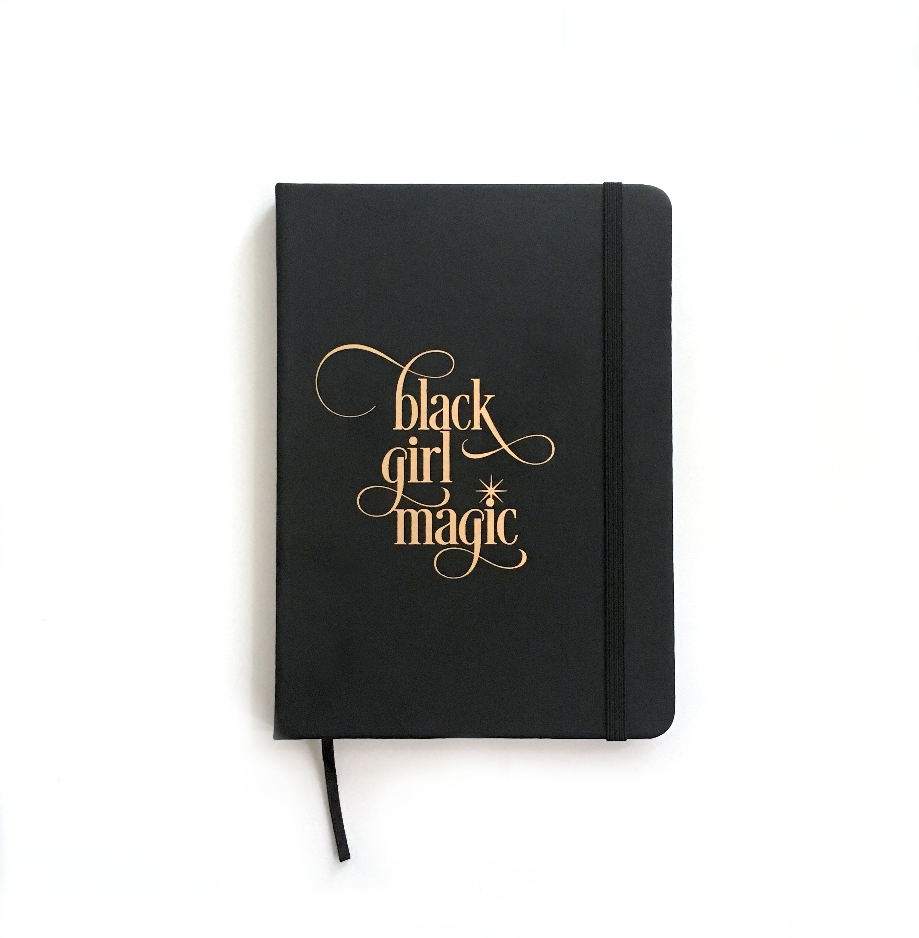 Black Girl Magic Notebook with soft PVC leather cover, gold writing, and elastic band closure, featuring 80 lined pages and a ribbon bookmark.