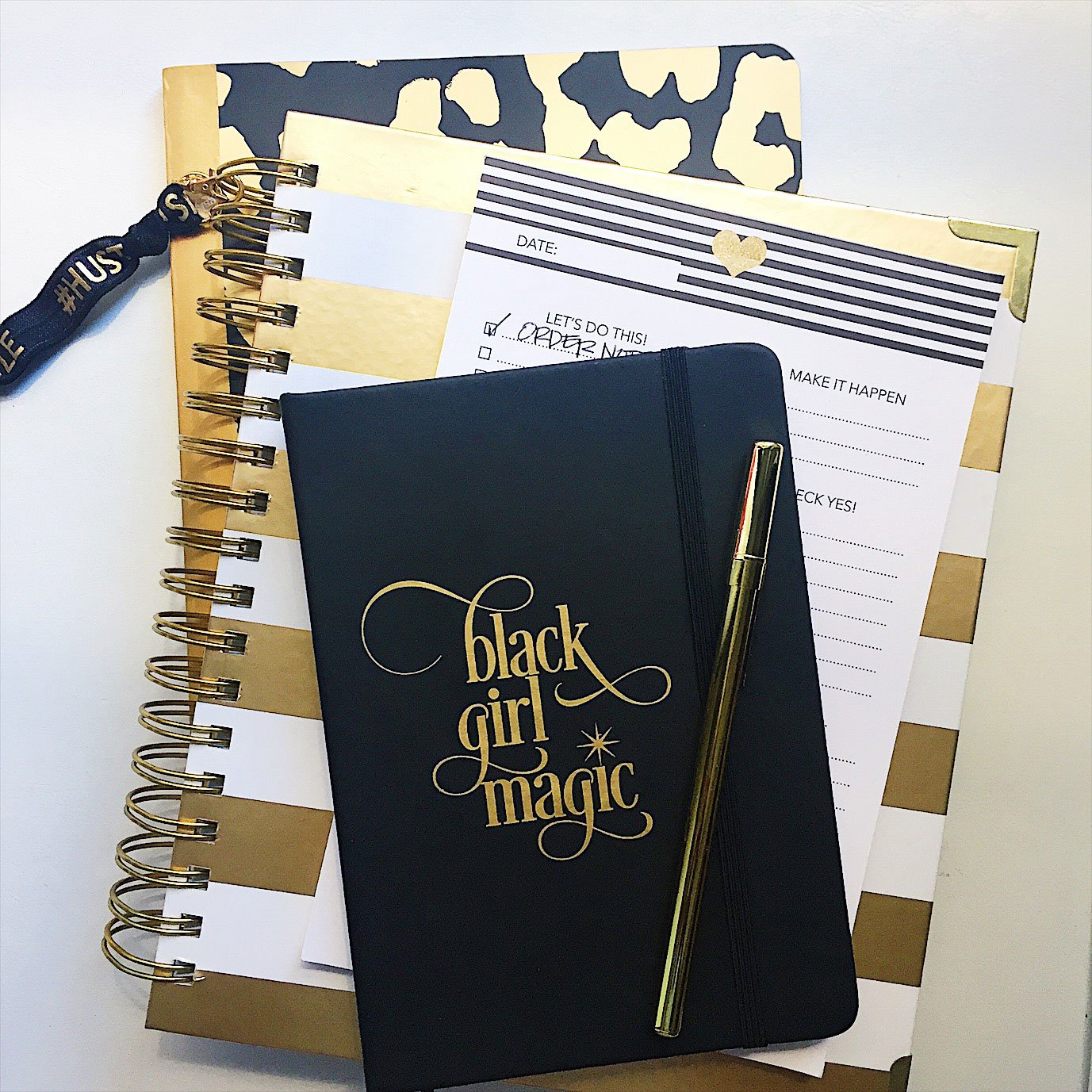 Black Girl Magic Notebook with soft PVC leather cover, gold writing, and elastic band closure, featuring 80 lined pages and a ribbon bookmark.