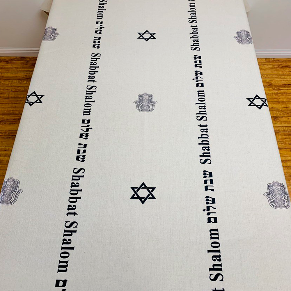 Elegant Black Shabbat Shalom tablecloth featuring Hebrew and English stripes, Magen David and Hamsa details, made from linen-cotton blend.