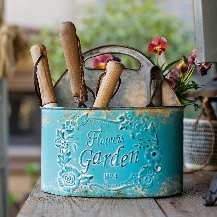 A vibrant turquoise blue metal basket tool organizer, perfect for storing gardening tools and accessories in a flower garden.