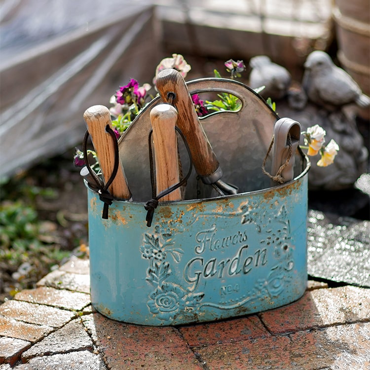 A vibrant turquoise blue metal basket tool organizer, perfect for storing gardening tools and accessories in a flower garden.