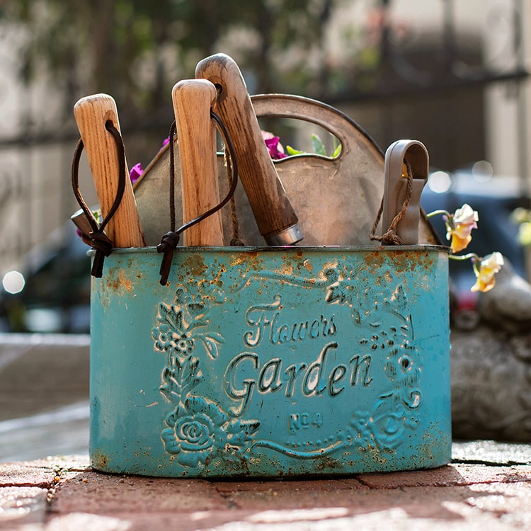 A vibrant turquoise blue metal basket tool organizer, perfect for storing gardening tools and accessories in a flower garden.