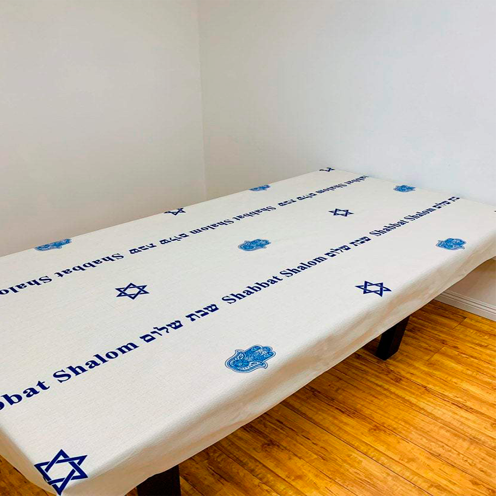 Blue Shabbat Shalom tablecloth featuring Hebrew and English stripes with Magen David and Hamsa designs, made from linen-cotton blend.