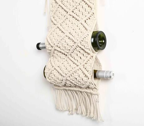 A stylish Bohemian Macrame Cotton Wine Rack holding three wine bottles, featuring intricate handmade knots and fringes on a wooden dowel.