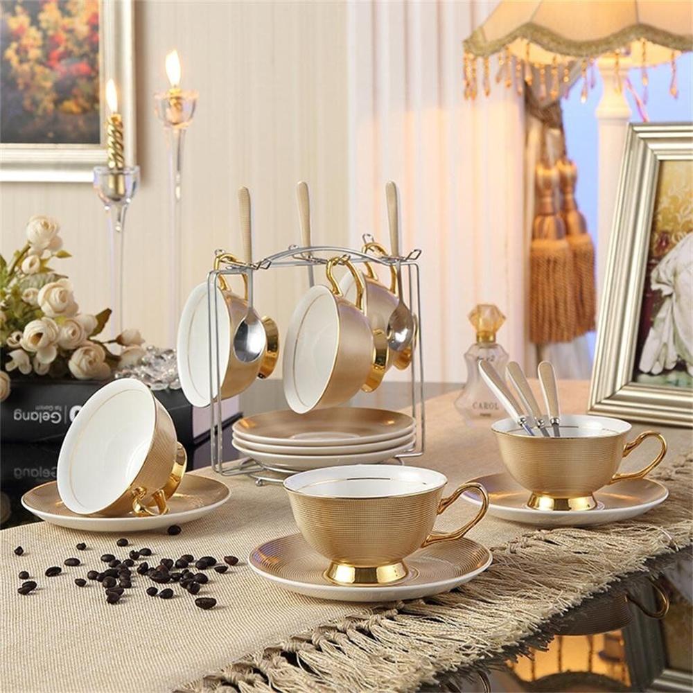 A beautifully arranged set of bone china teacups and saucers in various colors, including pink, green, black, and golden, accompanied by matching spoons.