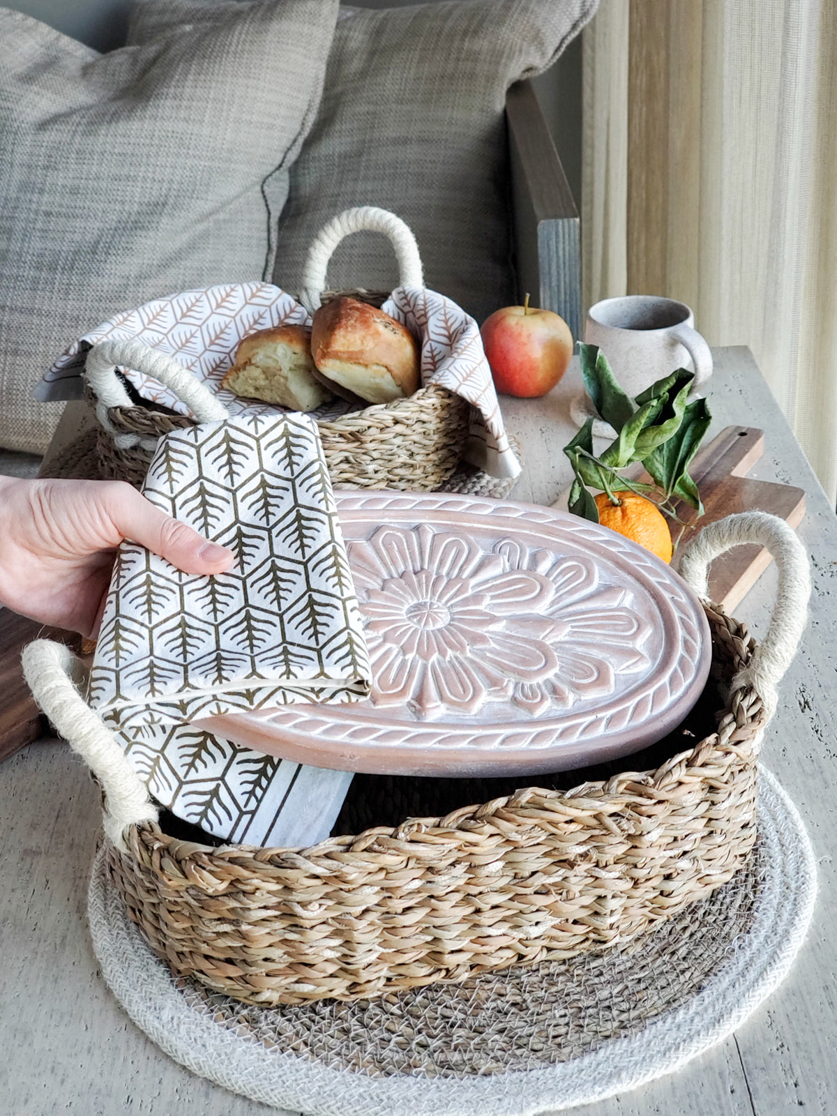 A beautifully crafted Flower Bread Warmer made of terracotta, placed inside a handwoven seagrass basket, showcasing intricate flower engravings.