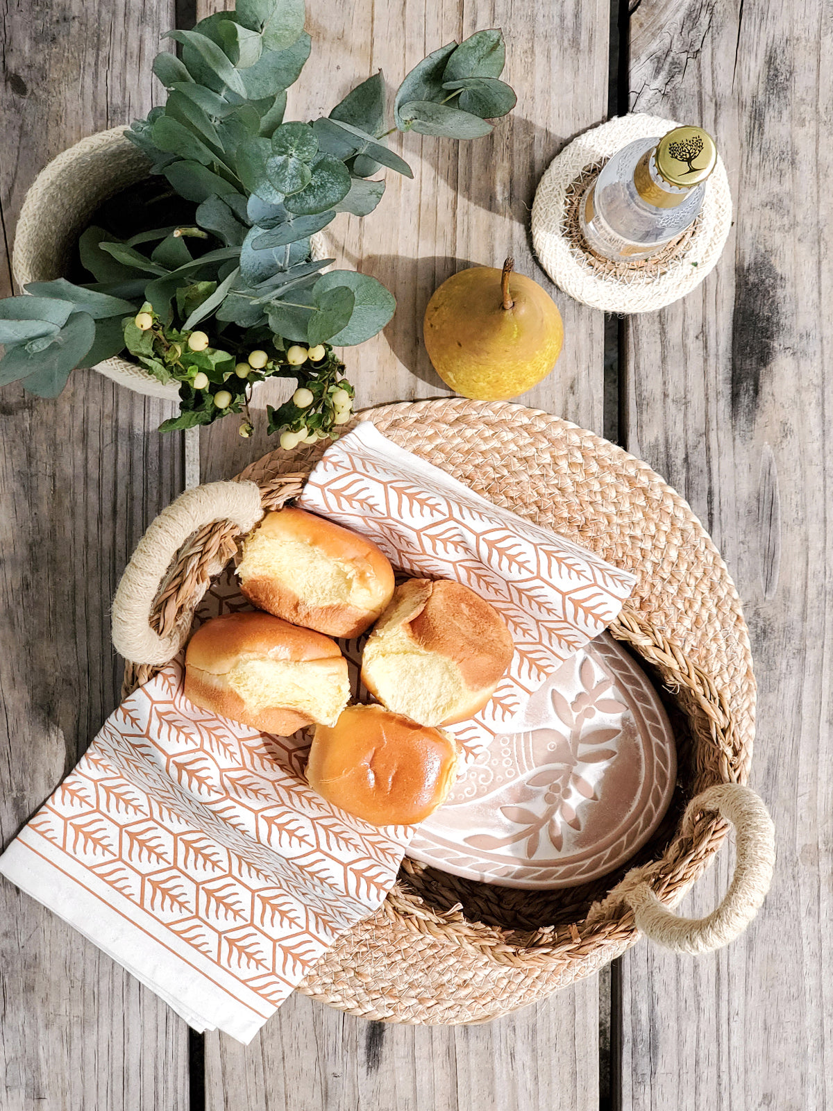 A beautifully crafted terracotta bread warmer with a bird design, accompanied by a handwoven seagrass basket and a natural cotton tea towel.