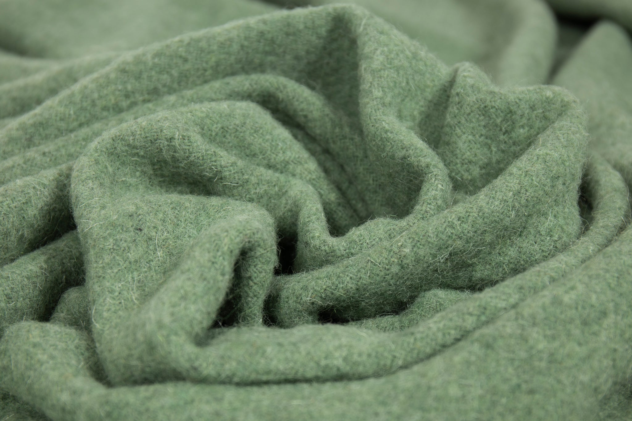 Brighton Throw blanket in sage color, made from 100% New Zealand wool, elegantly draped on a cozy sofa.