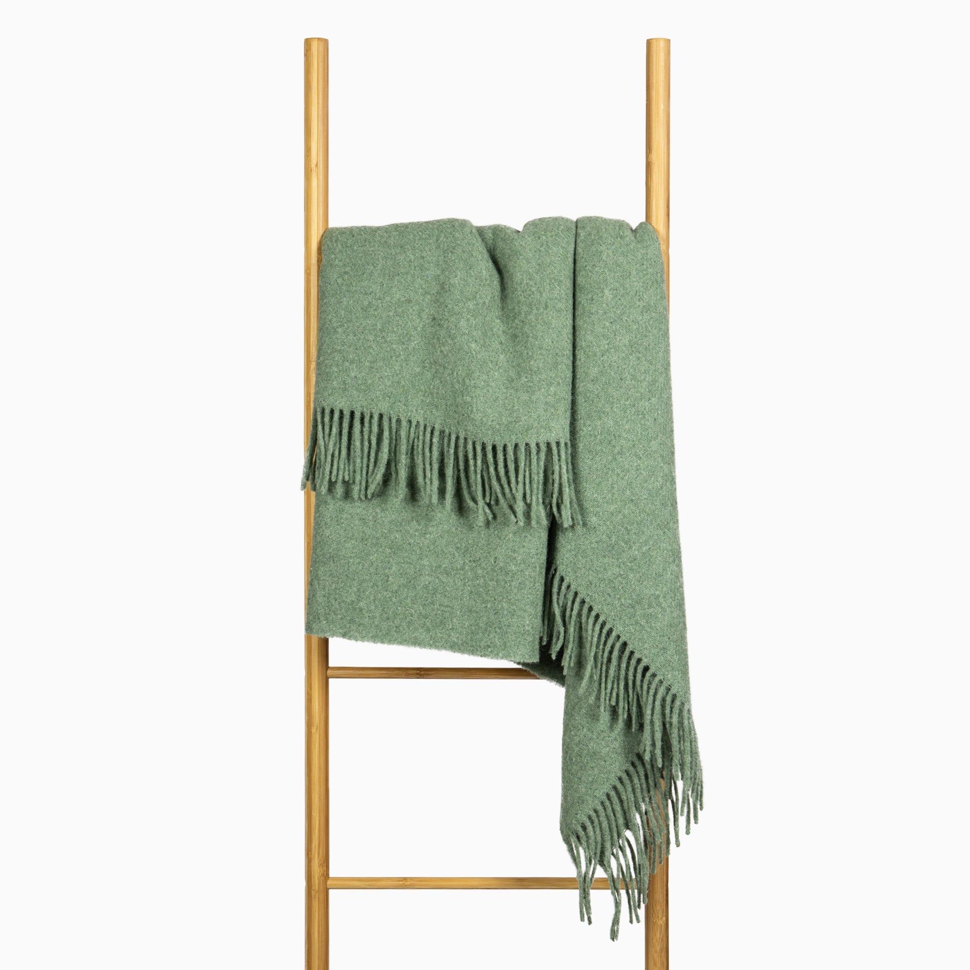 Brighton Throw blanket in sage color, made from 100% New Zealand wool, elegantly draped on a cozy sofa.