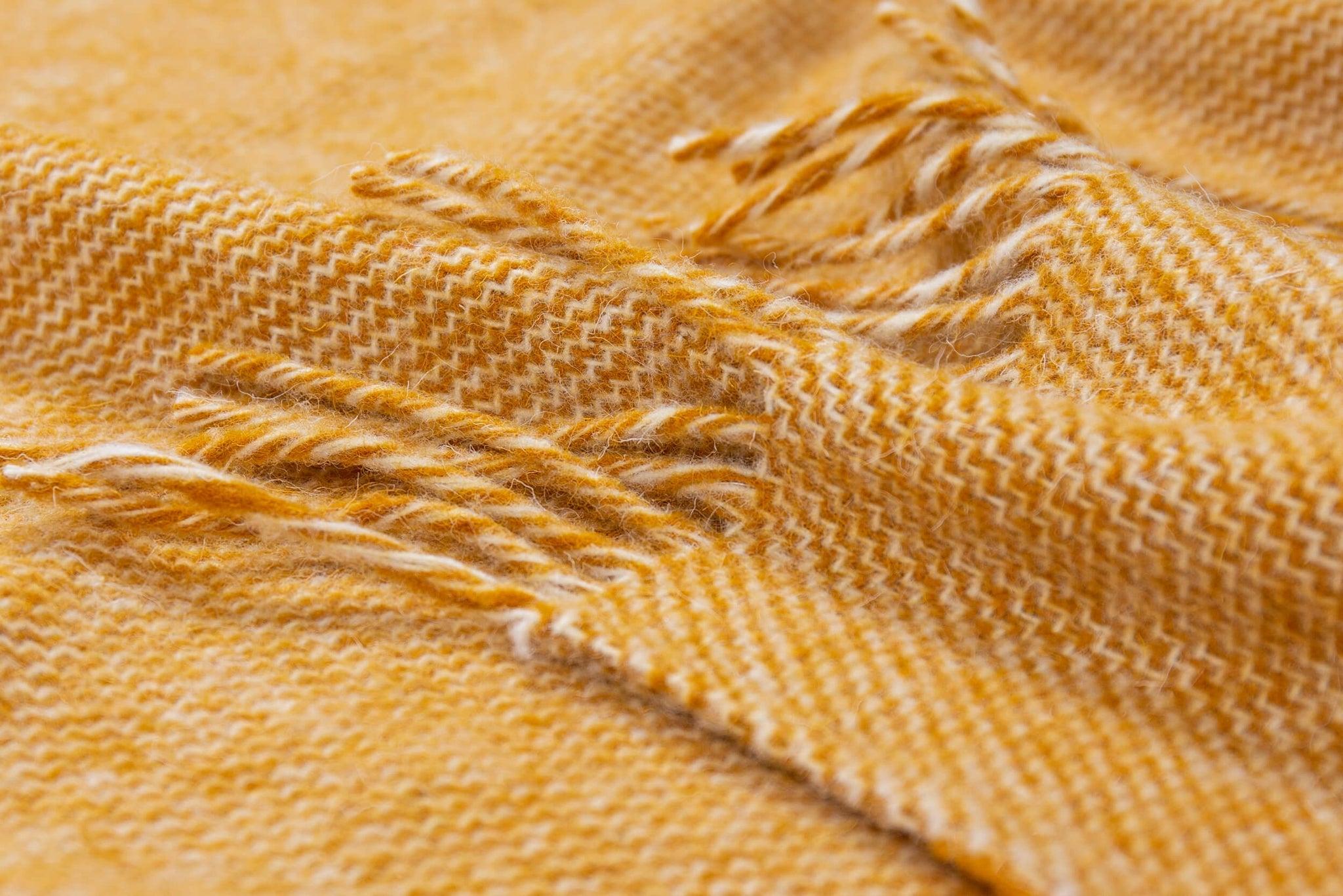 Cozy Cambridge Throw blanket made from 100% New Zealand wool in mustard color, elegantly draped on a sofa.