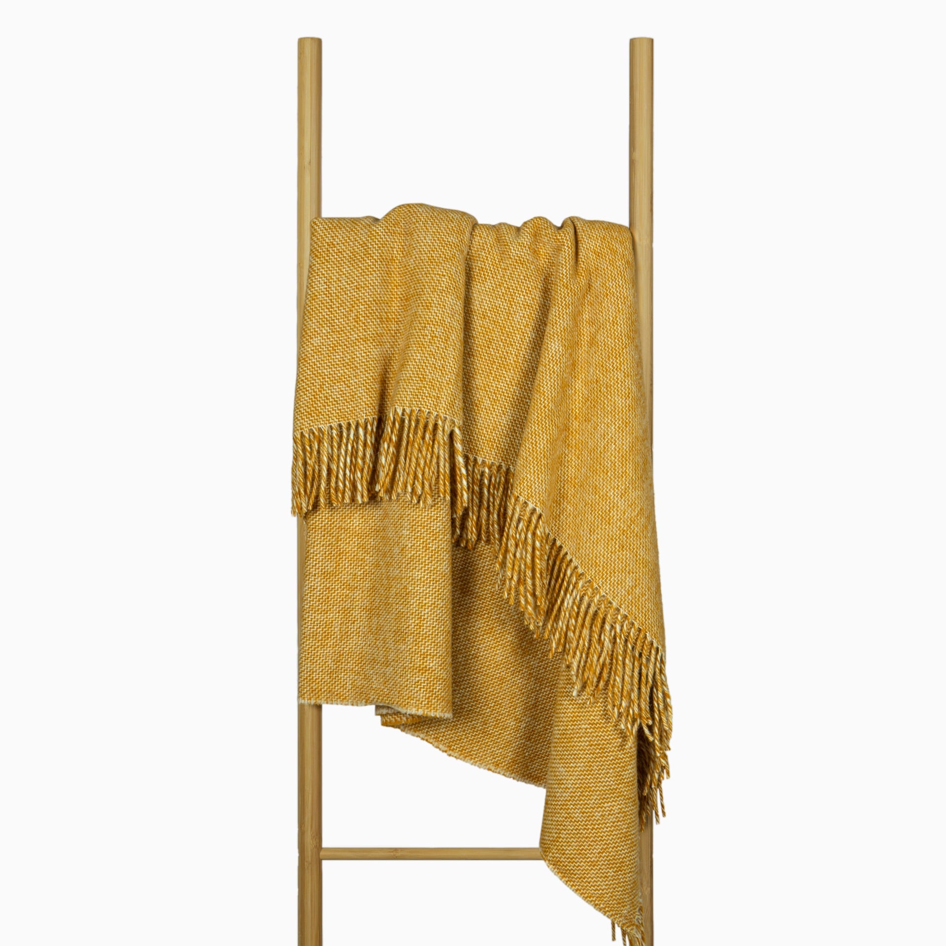 Cozy Cambridge Throw blanket made from 100% New Zealand wool in mustard color, elegantly draped on a sofa.