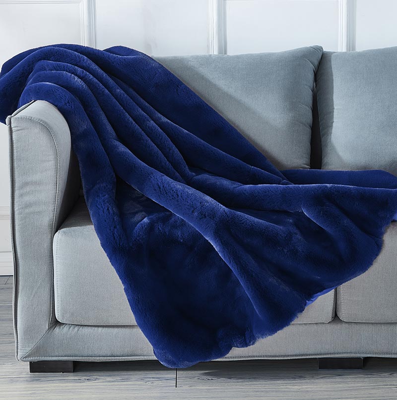 Cassilda Luxury Navy Blue Chinchilla Faux Fur Throw Blanket draped elegantly on a sofa, showcasing its plush texture and rich color.