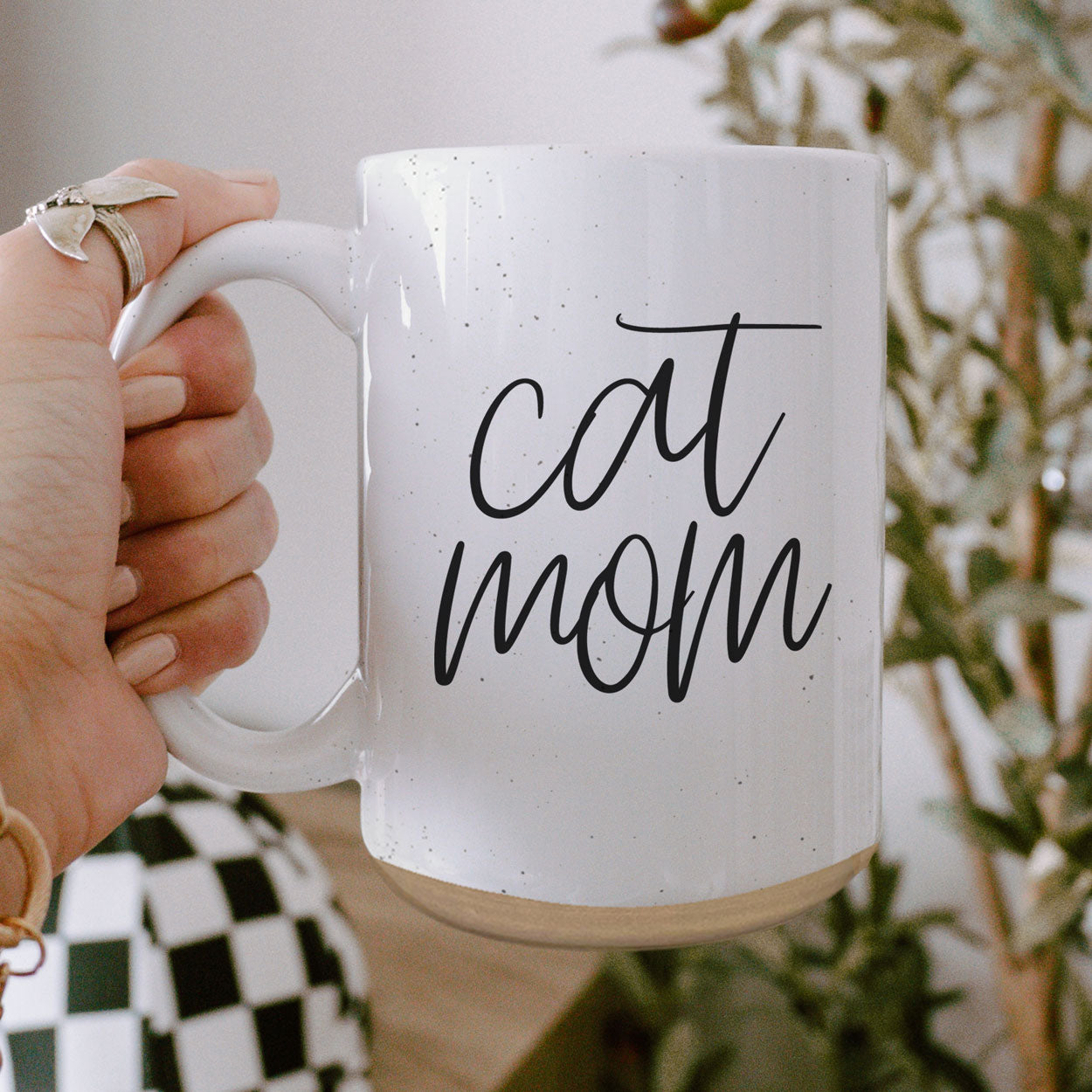 A stylish off-white ceramic mug with dark speckles, featuring a black graphic that reads 'Cat Mom' on both sides, perfect for cat lovers.