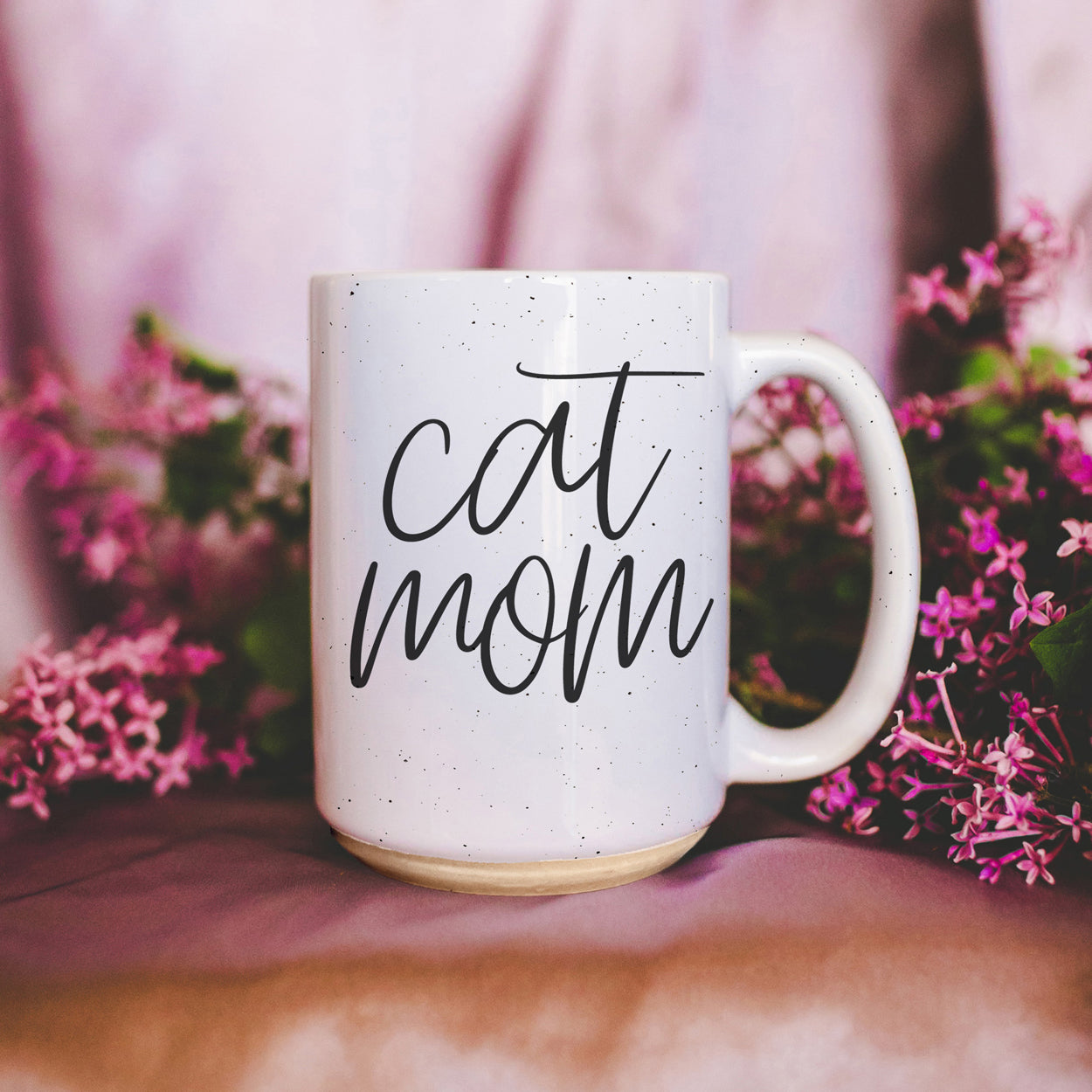 A stylish off-white ceramic mug with dark speckles, featuring a black graphic that reads 'Cat Mom' on both sides, perfect for cat lovers.