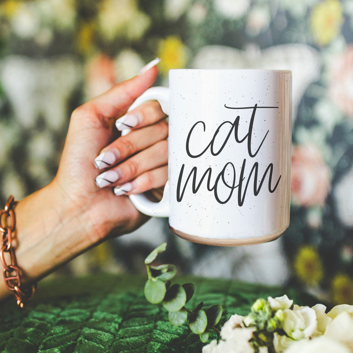 A stylish off-white ceramic mug with dark speckles, featuring a black graphic that reads 'Cat Mom' on both sides, perfect for cat lovers.