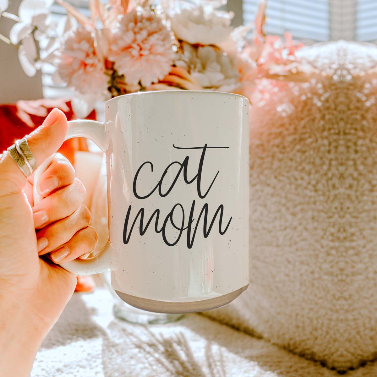 A stylish off-white ceramic mug with dark speckles, featuring a black graphic that reads 'Cat Mom' on both sides, perfect for cat lovers.