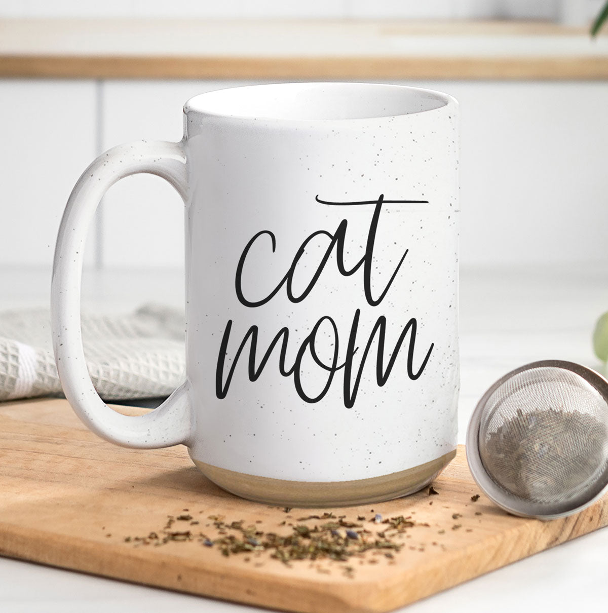 A stylish off-white ceramic mug with dark speckles, featuring a black graphic that reads 'Cat Mom' on both sides, perfect for cat lovers.