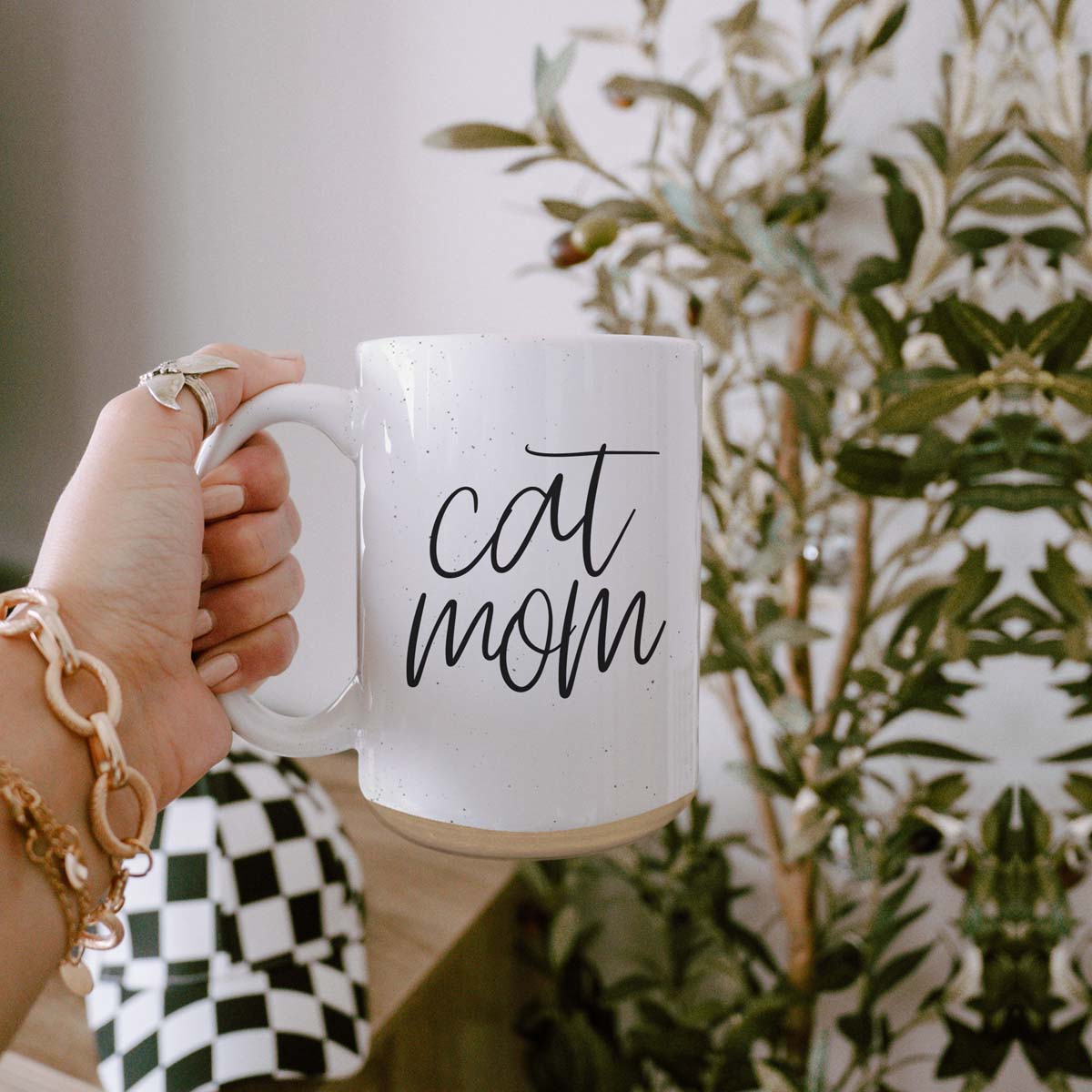 A stylish off-white ceramic mug with dark speckles, featuring a black graphic that reads 'Cat Mom' on both sides, perfect for cat lovers.