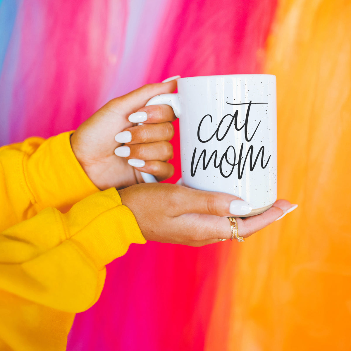 A stylish off-white ceramic mug with dark speckles, featuring a black graphic that reads 'Cat Mom' on both sides, perfect for cat lovers.