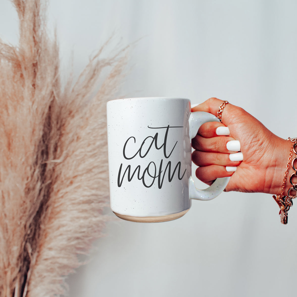 A stylish off-white ceramic mug with dark speckles, featuring a black graphic that reads 'Cat Mom' on both sides, perfect for cat lovers.