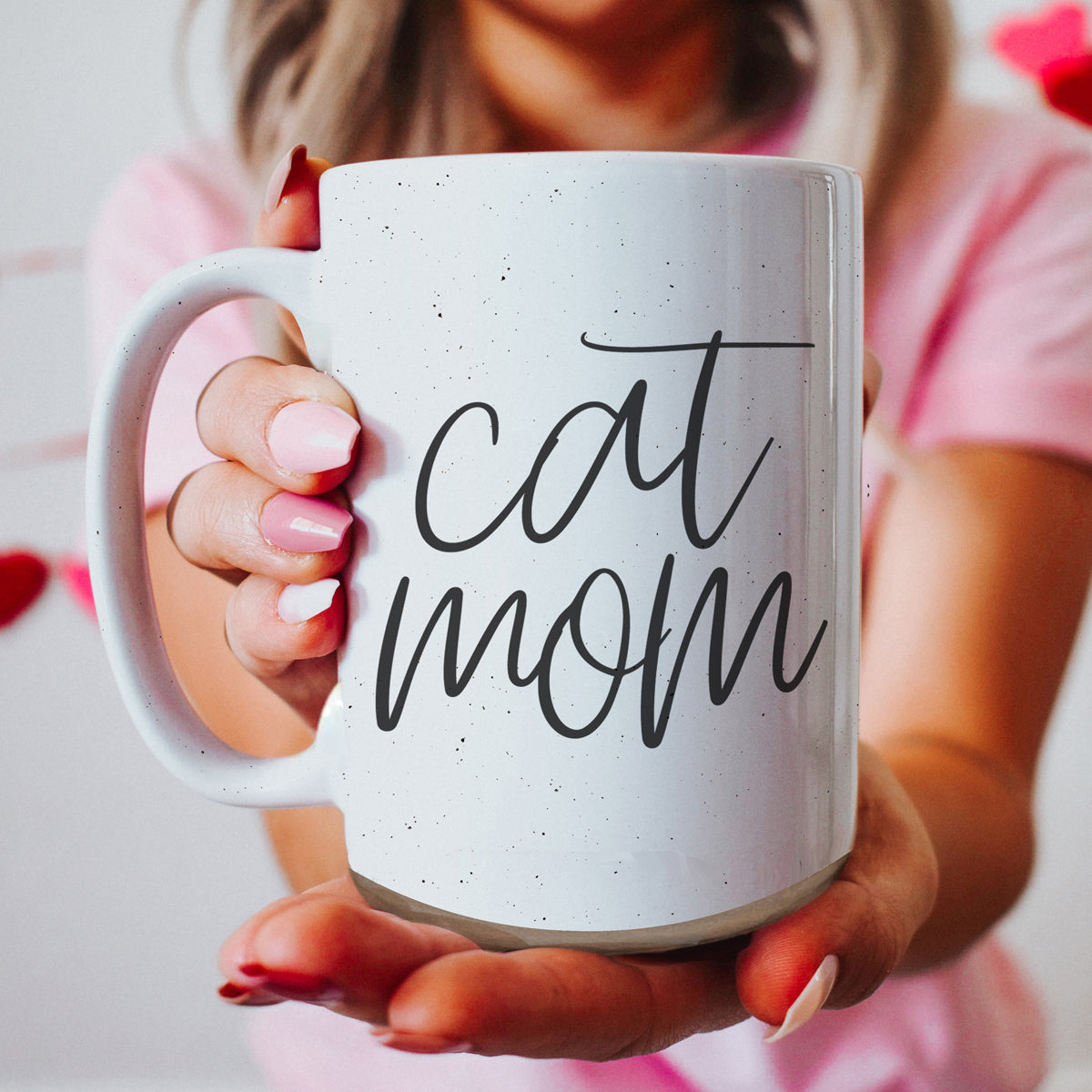 A stylish off-white ceramic mug with dark speckles, featuring a black graphic that reads 'Cat Mom' on both sides, perfect for cat lovers.