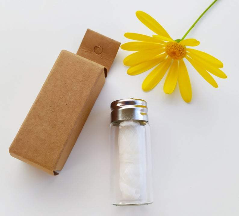 A glass bottle containing biodegradable charcoal dental floss, showcasing its eco-friendly packaging and spearmint flavor.