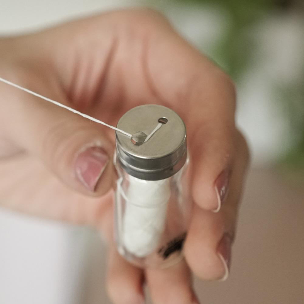 A glass bottle containing biodegradable charcoal dental floss, showcasing its eco-friendly packaging and spearmint flavor.