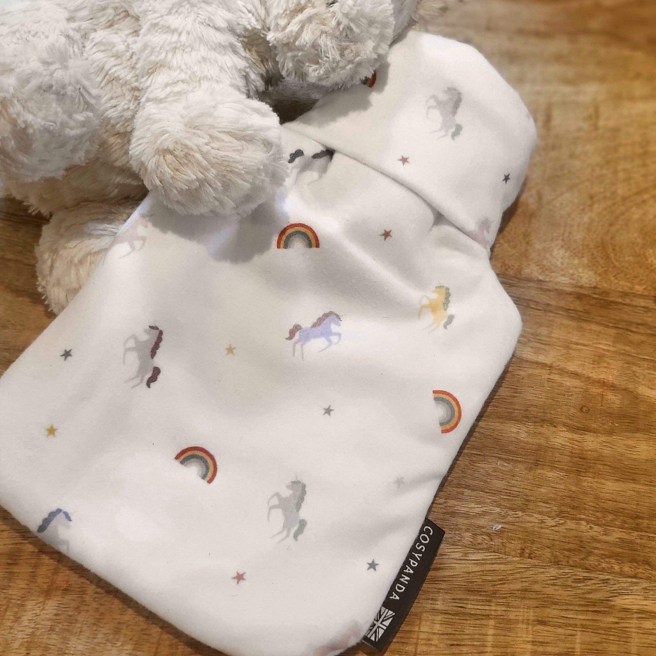 A soft children's hot water bottle featuring a colorful unicorn rainbow print, designed for comfort and safety.