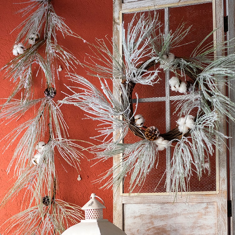 A beautifully crafted Christmas Faux Snow Pine Needle Wreath made from natural rattan, adorned with pine cones and cotton, showcasing a wintery aesthetic.