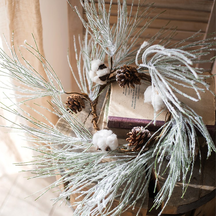 A beautifully crafted Christmas Faux Snow Pine Needle Wreath made from natural rattan, adorned with pine cones and cotton, showcasing a wintery aesthetic.