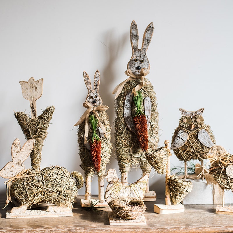 A collection of rustic Christmas figurine decorations including a hen, owl, rabbit, and flowers, crafted from natural wood and straw.